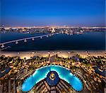 Cityscape of Dubai, United Arab Emirates at dusk, with bridge from  island across the Persian Gulf in the foreground.