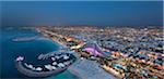 Cityscape of Dubai, United Arab Emirates at dusk, with coastline of Persian Gulf and marina in the foreground.