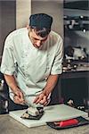 Food concept. One young white chef dressed in white uniform decorate ready dish in restaurant. He is working on maki rolls. Preparing traditional japanese sushi set in interior of modern kitchen