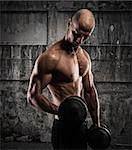 Athletic muscular man training biceps with dumbbells on grunge background