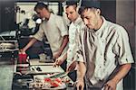 Food concept. Three young chefs in white uniform decorate ready dish in restaurant. They are working on maki rolls. Preparing traditional japanese sushi set in interior of modern professional kitchen