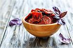 Sun-dried tomatoes and purple basil in a bowl on wooden table, selective focus.
