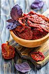 Sun-dried tomatoes and red basil in bowl, on wooden table, selective focus.