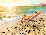 Girl tans on a deck chair on a beautiful beach during sunset