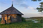 Landscape with an old wooden chapel at sunset against a background of a green meadow and a river