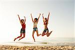 Happy smiling friends jumping over the sea