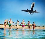 Group of friends run in the blue sea with aircraft in the sky. Concept of summertime