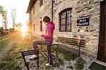 Grazzano Visconti, Vigolzone, Piacenza district, Emilia Romagna, Italy. Woman reading on a chair in a old couryard of the town.