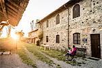 Grazzano Visconti, Vigolzone, Piacenza district, Emilia Romagna, Italy. Woman reading on a chair in a old couryard of the town.