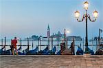 A solitary man is waiting in front of the gondolas docked along the Riva degli Schiavoni. in the background the island of San Giorgio Maggiore, Venice, Italy