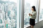 Businesswoman with smartphone looking out of window