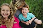 Portrait of girl and brother sitting on mothers lap in grass