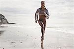 Front view of young female runner running barefoot along beach