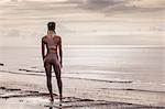 Rear view of young female runner at water's edge looking out to sea