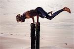 Young man training, doing handstand on wooden beach posts