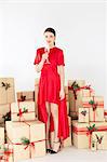 Portrait of young woman in red dress by stacked christmas gifts holding champagne