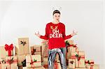 Portrait of young woman in red sweater and reindeer antlers posing by stacked christmas gifts