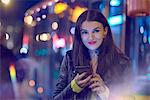 Young woman outdoors at night, holding smartphone, tattoos on hand and neck