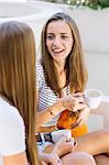 Two young female friends chatting at sidewalk cafe