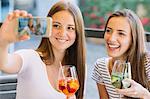 Two young female friends taking smartphone selfie at sidewalk cafe
