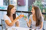 Two young female friends raising a cocktail toast at sidewalk cafe