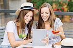 Two young female friends looking and laughing at digital tablet at sidewalk cafe