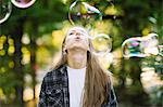 Young woman blowing floating bubble upwards in park