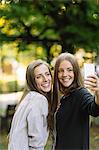Two young female friends posing for smartphone selfie in park