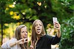 Two young female friends pulling faces for smartphone selfie in park