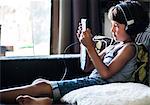 Boy sitting on sofa listening to headphones and staring at digital tablet