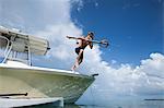 Man jumping into water from boat, carrying fishing spear