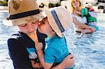 Family in outdoor swimming pool, young boy holding younger brother