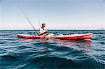 Young male sea kayaker looking at smartphone while fishing, Santa Cruz Island, California, USA
