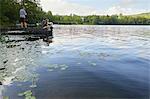 Three children on jetty beside lake, young boy fishing using fishing rod