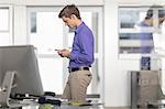 Young male office worker looking at smartphone in office