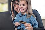 Girl and mother on sofa using laptop and credit card for online shopping