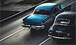 High angle shot of two classic 1950s cars driving on a road.