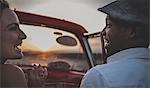 Two people riding in an open convertible classic car looking at each other and smiling.