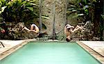 Two children in mid air, somersaulting backwards into a swimming pool.