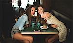 Two young women sitting at a cafe table posing for a selfie.