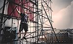 Young man standing on scaffolding on the outside of a city building.