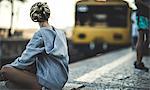 Young woman sitting on a railway station platform with a train behind.