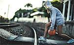 Young woman running across railway tracks bouncing a basketball.
