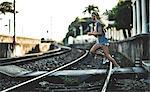 Young woman running across railway tracks holding a basketball.