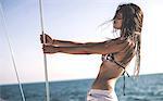 A young woman on board a yacht, side view in bikini and shorts.