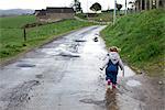 Little girl walking along wet dirt road