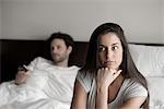 Woman sitting in bed while husband watching tv