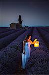Woman with lantern at dawn in a lavender field. Plateau de Valensole, Alpes-de-Haute-Provence, Provence-Alpes-Côte d'Azur, France, Europe.