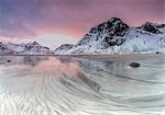 Pink sky on the surreal Skagsanden beach surrounded by snow covered mountains. Lofoten Islands Northern Norway Europe