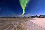 The aurora borealis lights up the sky and the beach of the cold sea of Gymsøyand. Lofoten Islands Northern Norway Europe